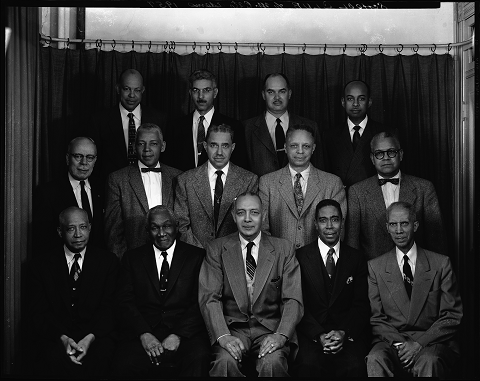 Black-and-white photo of three rows of men wearing suits and ties. They are sitting for a group portrait in the Scurlock Studio