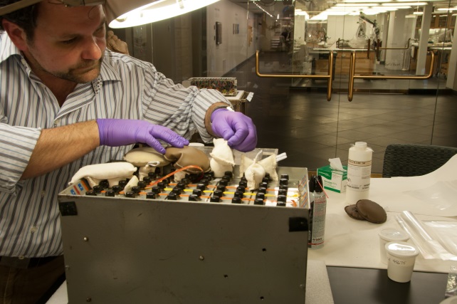Conservator Shockey stabilizing detached self-adhesive tape on the video analyzer. Image at right: Removing surface dirt from the audio synthesizer using carbon dioxide snow. 