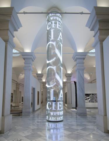 Gallery hallway with cylindrical tower made of lights displaying text