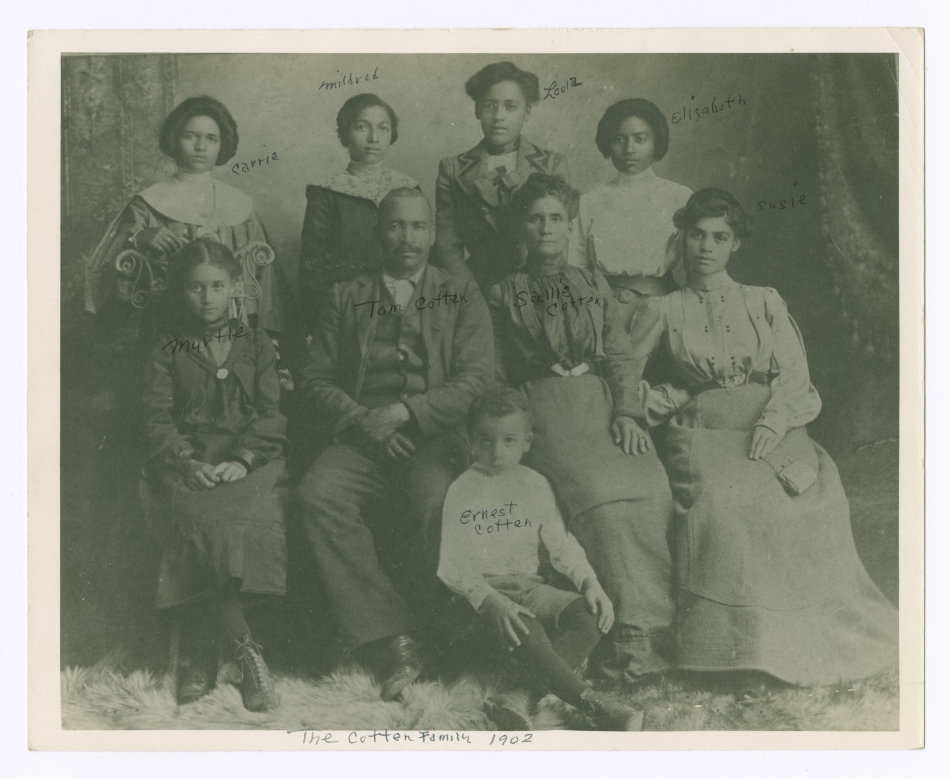 A black and white photograph of a family with a man and woman seated at the center. Six girls and one boy surround them.