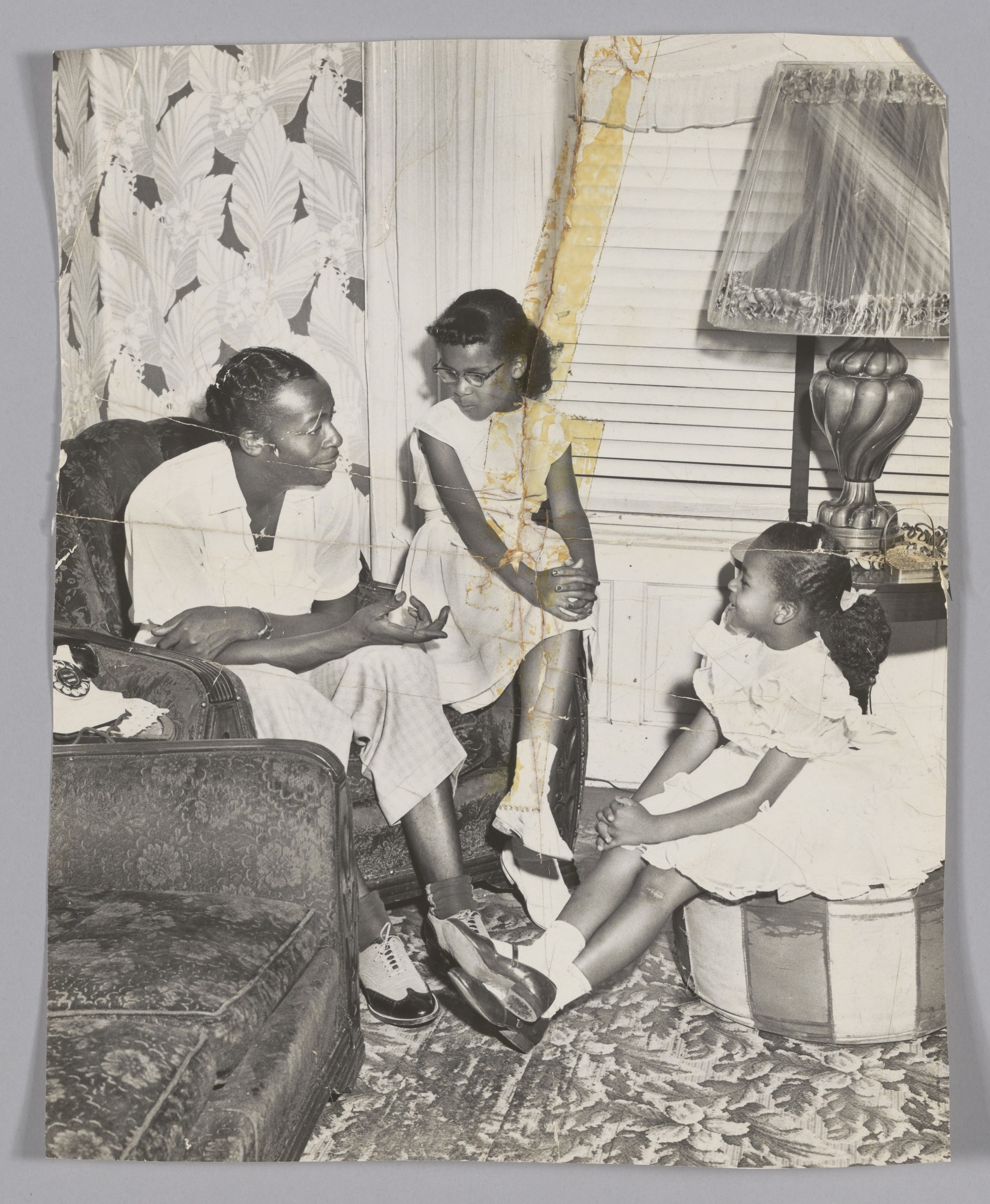 A man and two girls are seated in a living room. He is speaking to them.