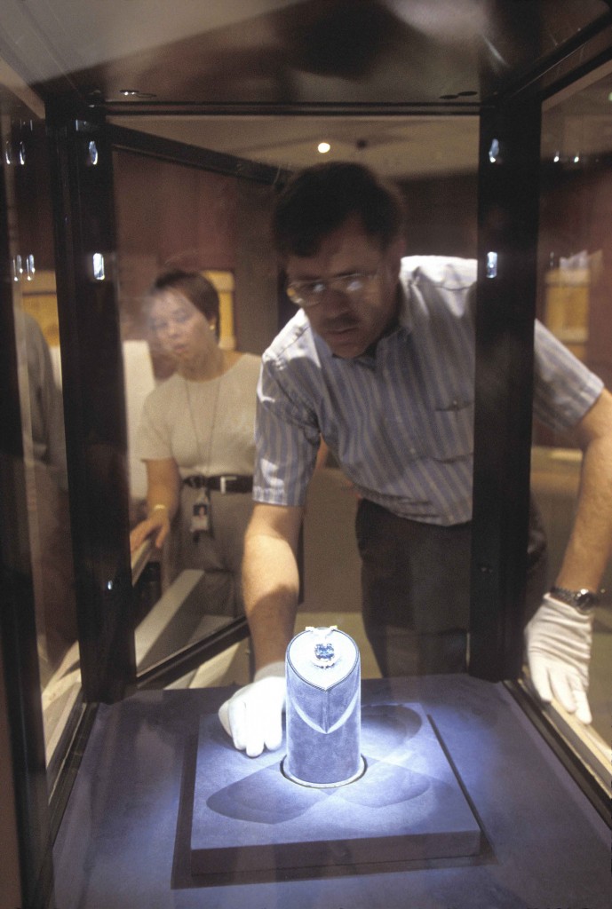 Photo: Photographed through the thick protective glass of the Hope Diamond’s exhibition case, Jeffrey Post returns the diamond to its pedestal in the Harry Winston Gallery of The Janet Annenberg Hooker Hall of Geology, Gems, and Minerals in the Smithsonian’s National Museum of Natural History. (Photos by Chip Clark)