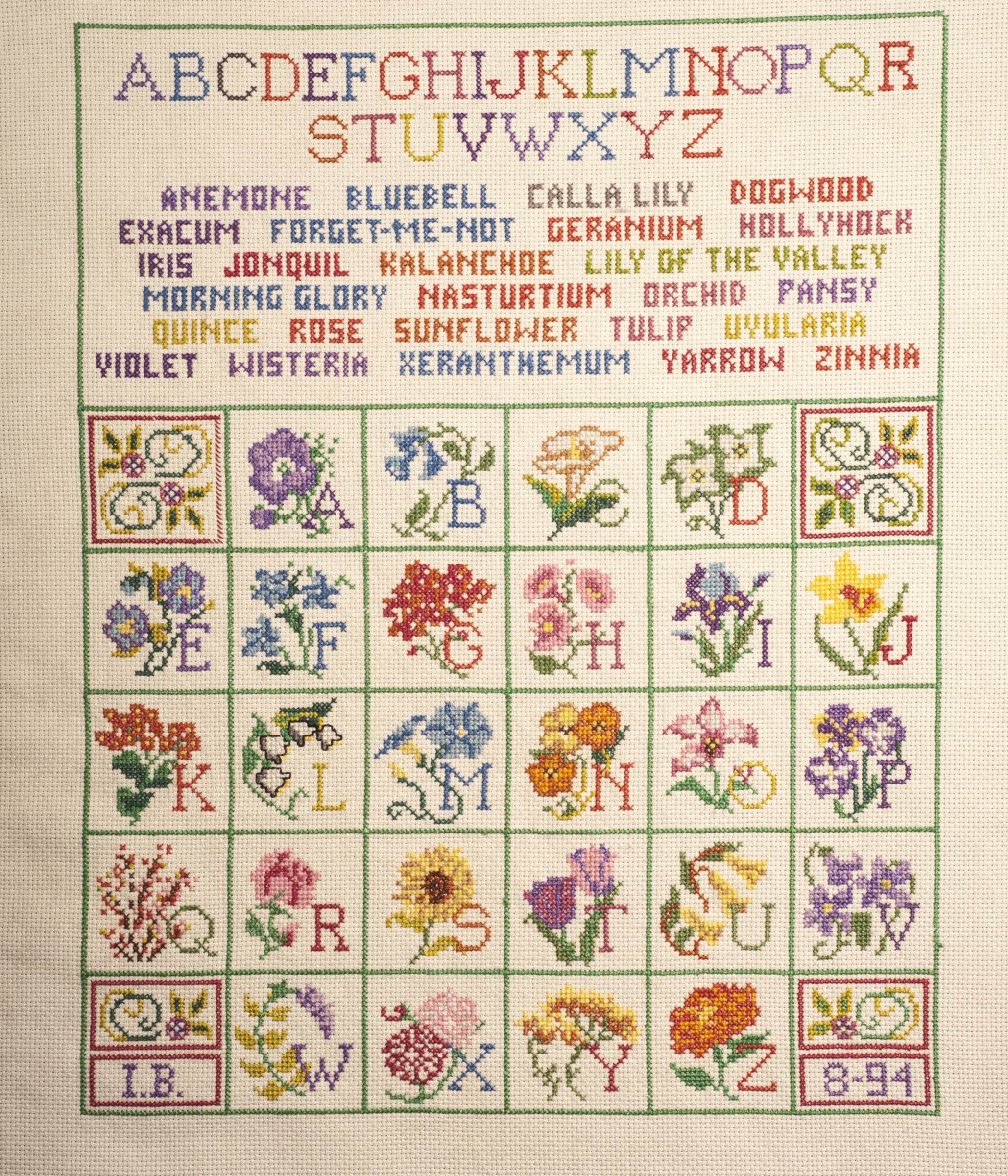 Colorful cross-stitch sampler. The alphabet and names of flowers are sewn across the top. Under that is a grid of letters paired with different flowers.