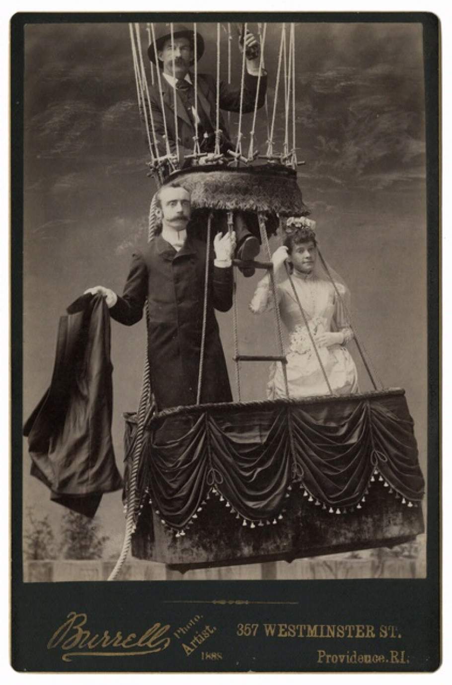 A couple stands in the basket attached to strings for a balloon.