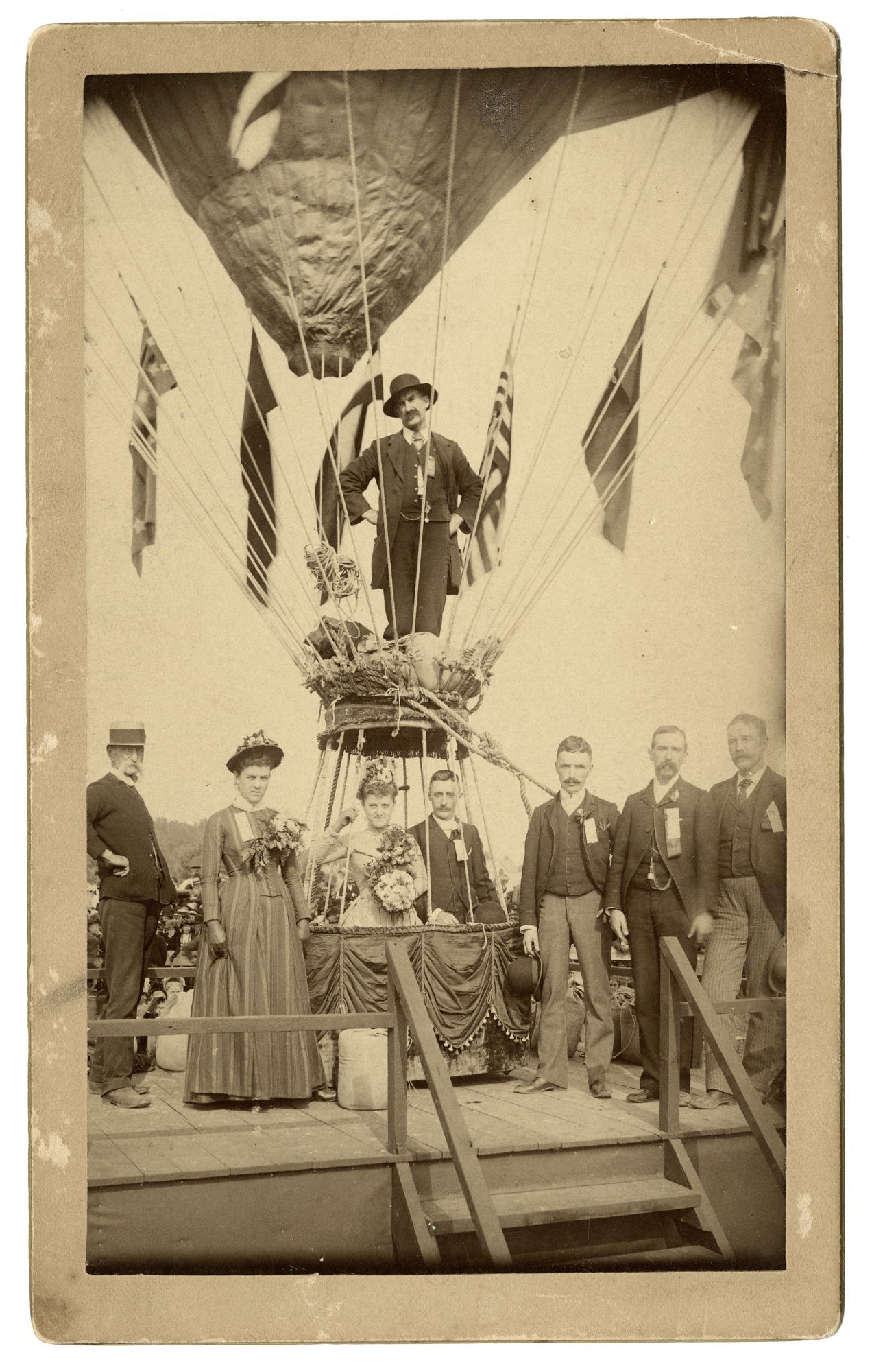 A group stands at a large balloon. A couple is in the basket, with another man standing above them.