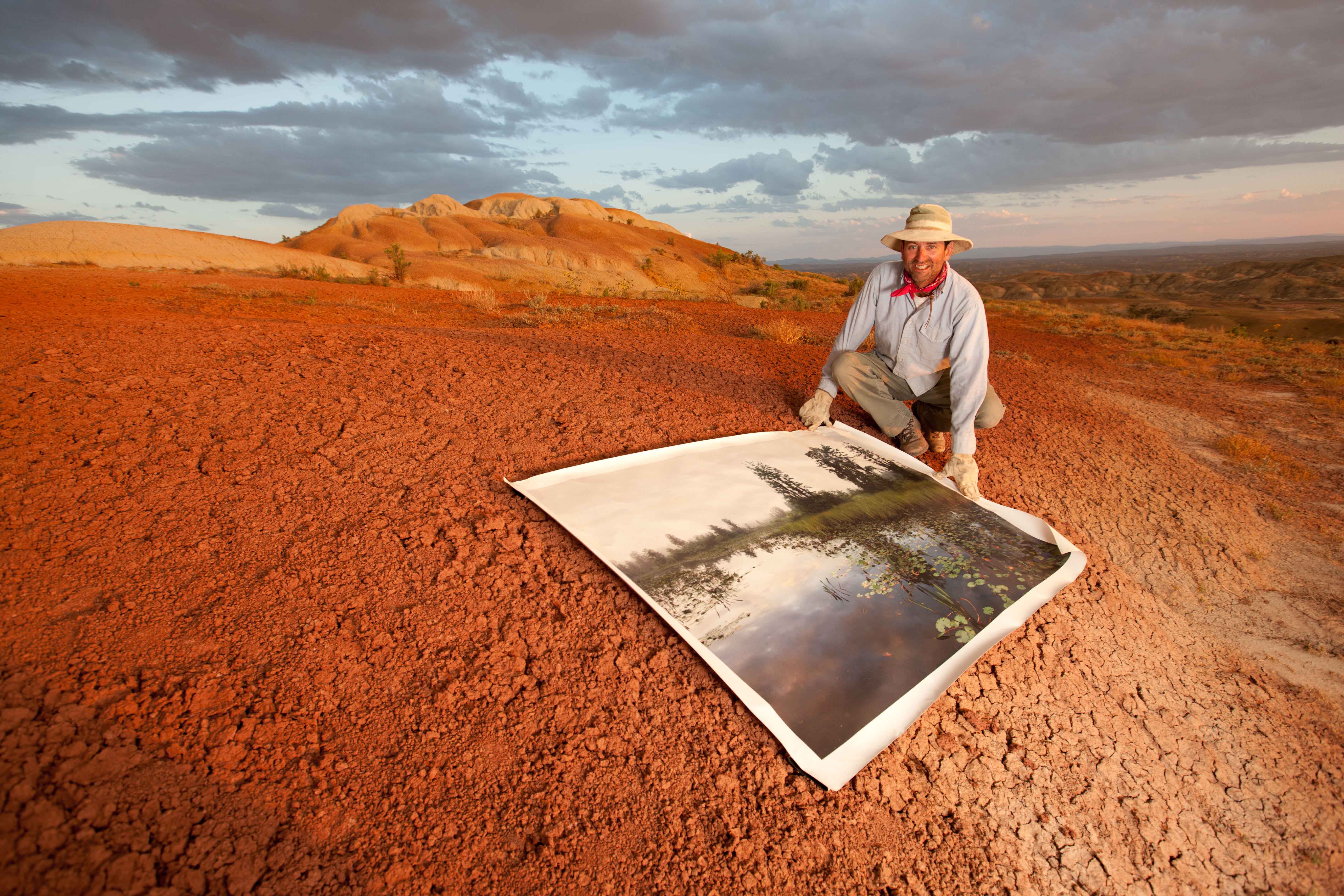 man in red soil holding a picture of a swamp