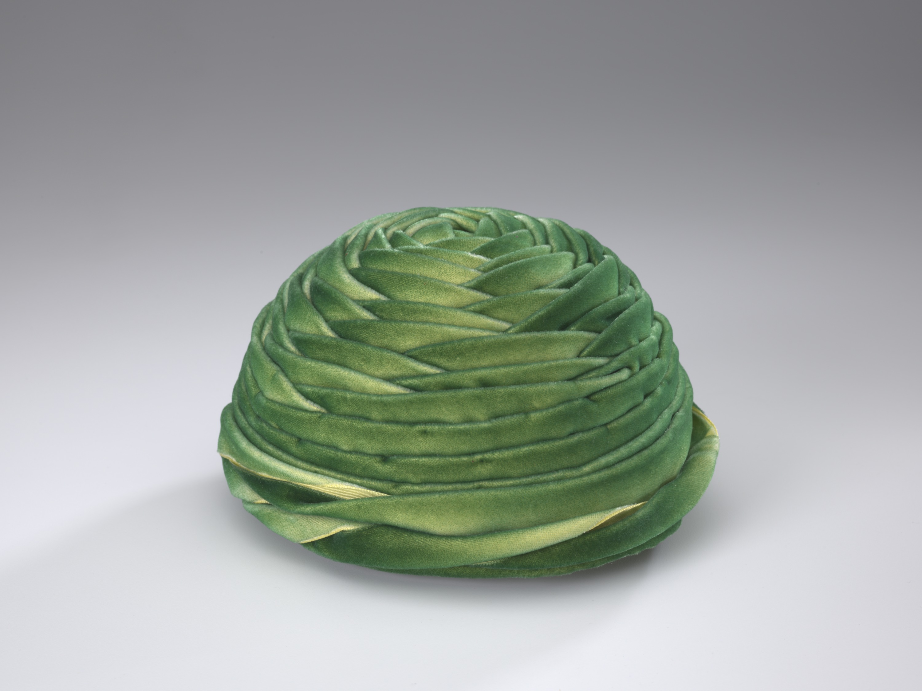 Green velveteen hat. It is circular with layers of fabric in a wrapped design.