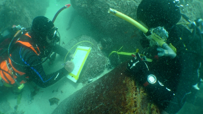 Two scuba divers underwater with sunken artifacts