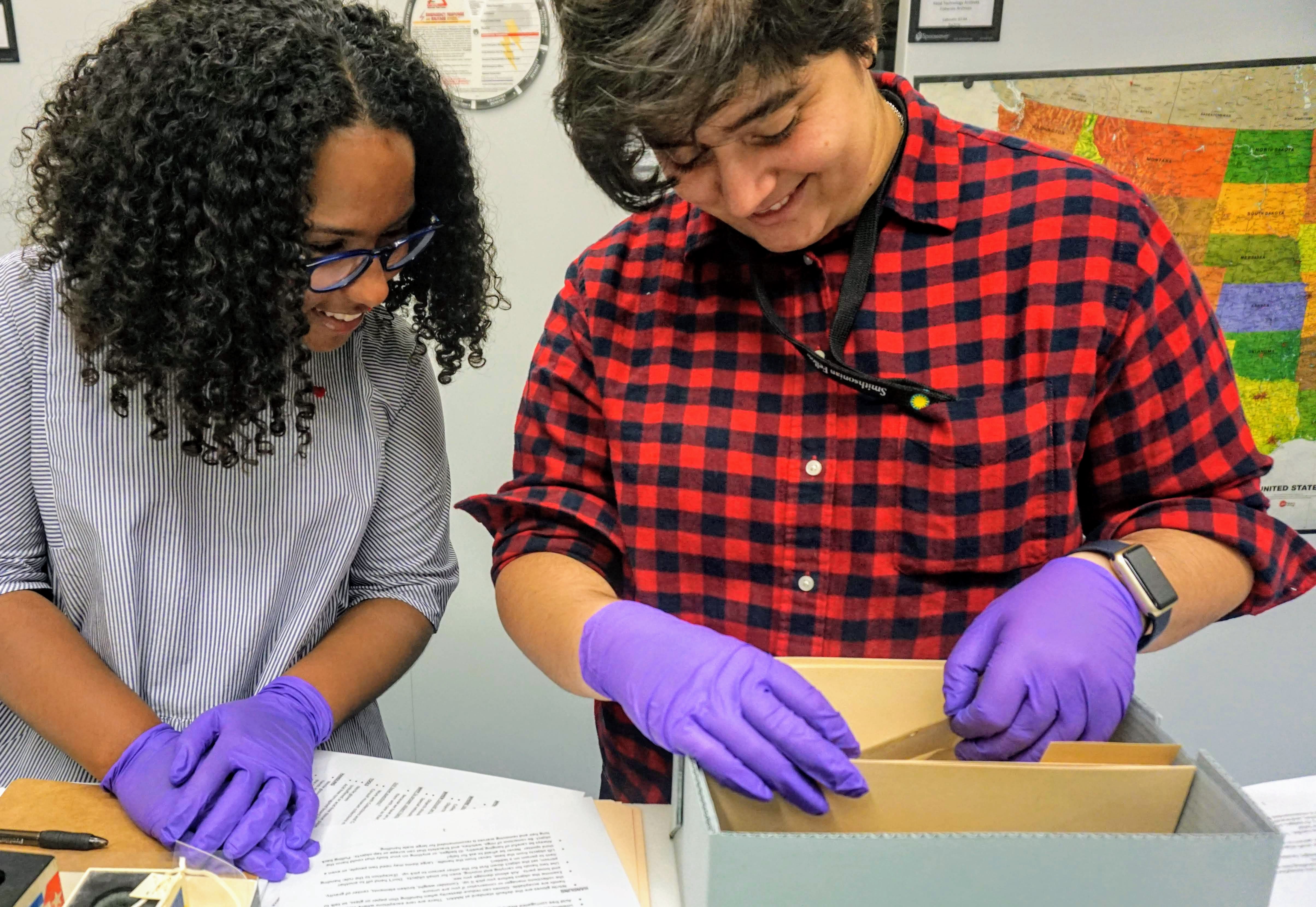 Deux jeunes adultes sourient en regardant dans une boîte d'archives