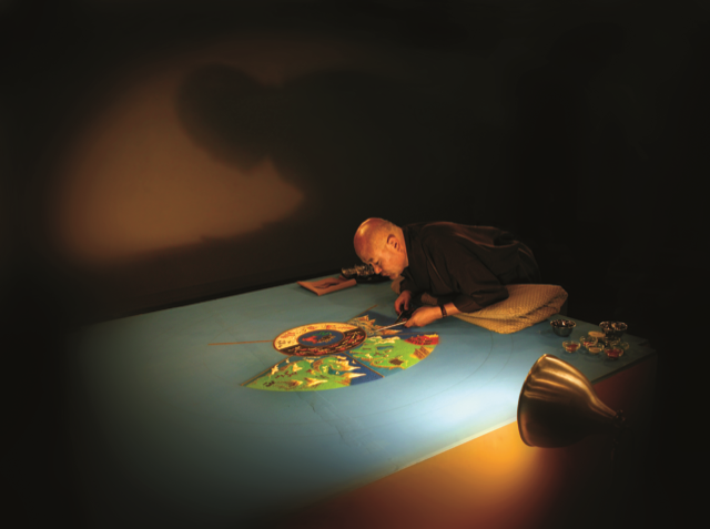 Artistically lit photo of monk creating sand mandala