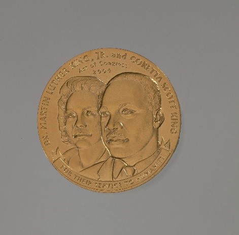 Circular gold medal with engraving of a man and womans faces.