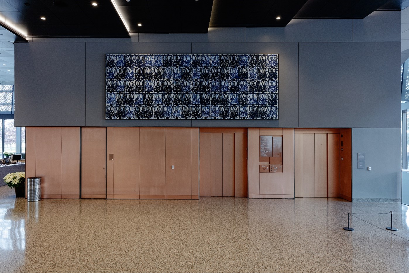 Black and blue patterned painting hangs above doorways and elevators in museum lobby.