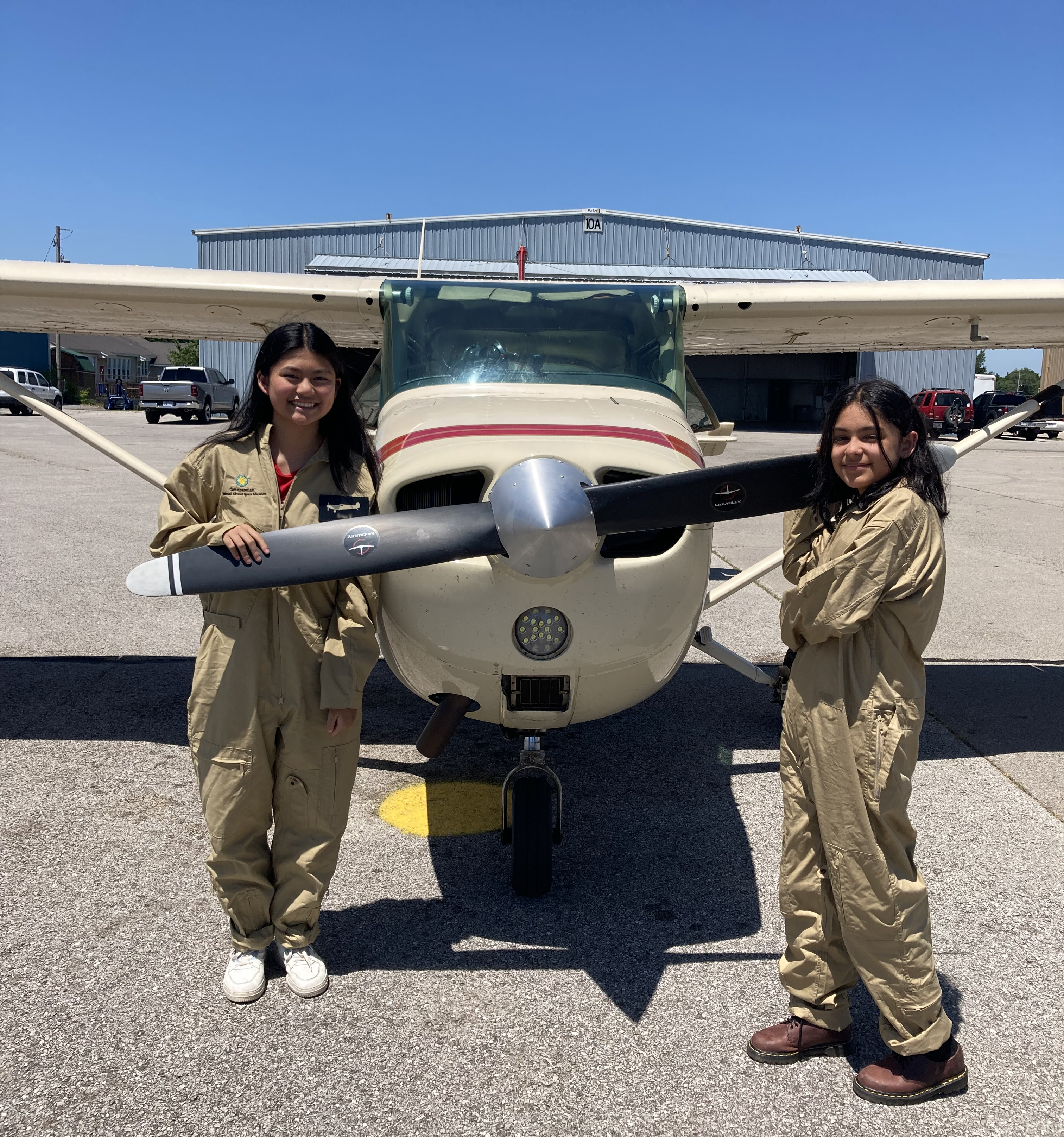 Two teenagers stand outside next to small plane and its propellers