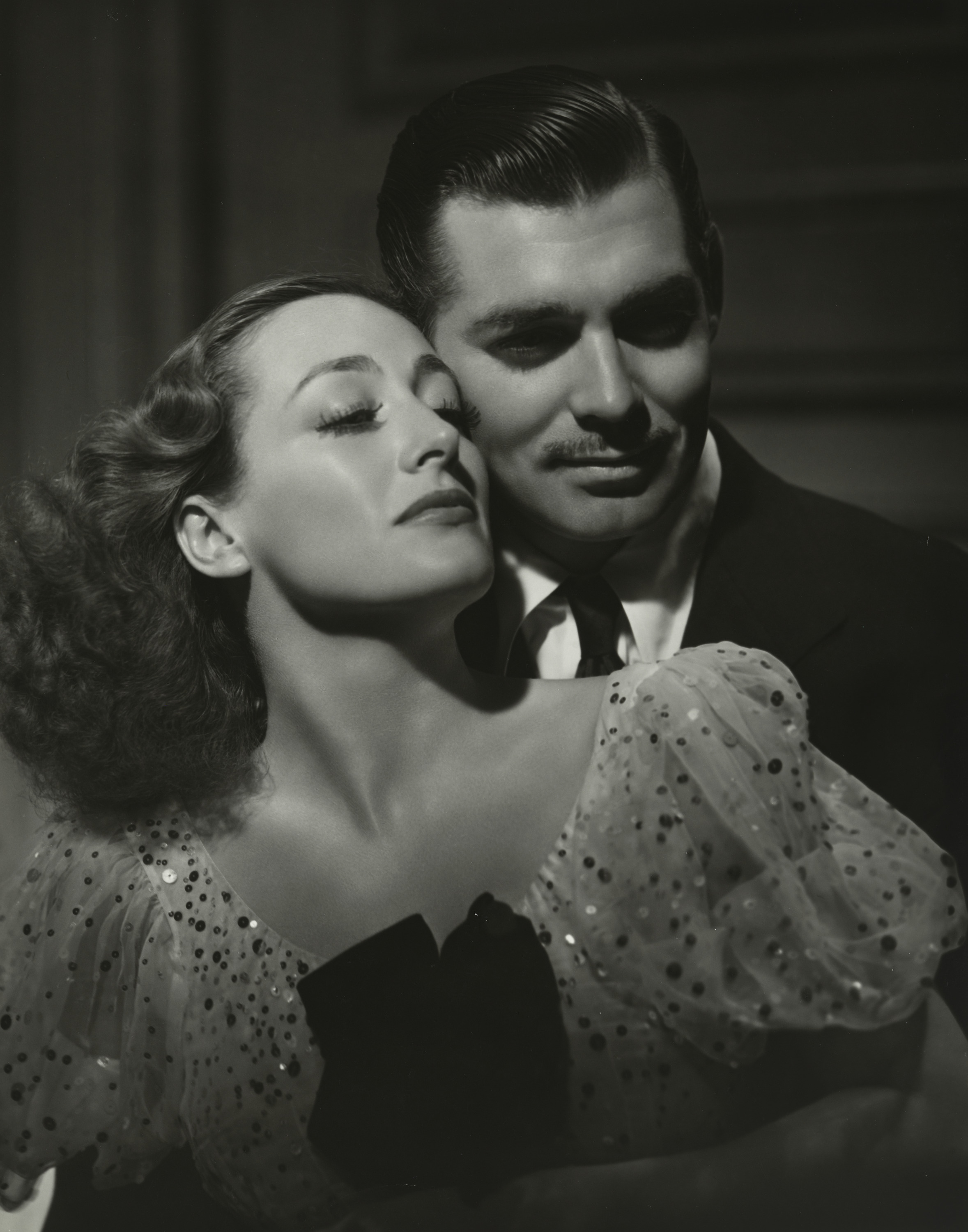 A man embraces a woman from behind in a black and white image.