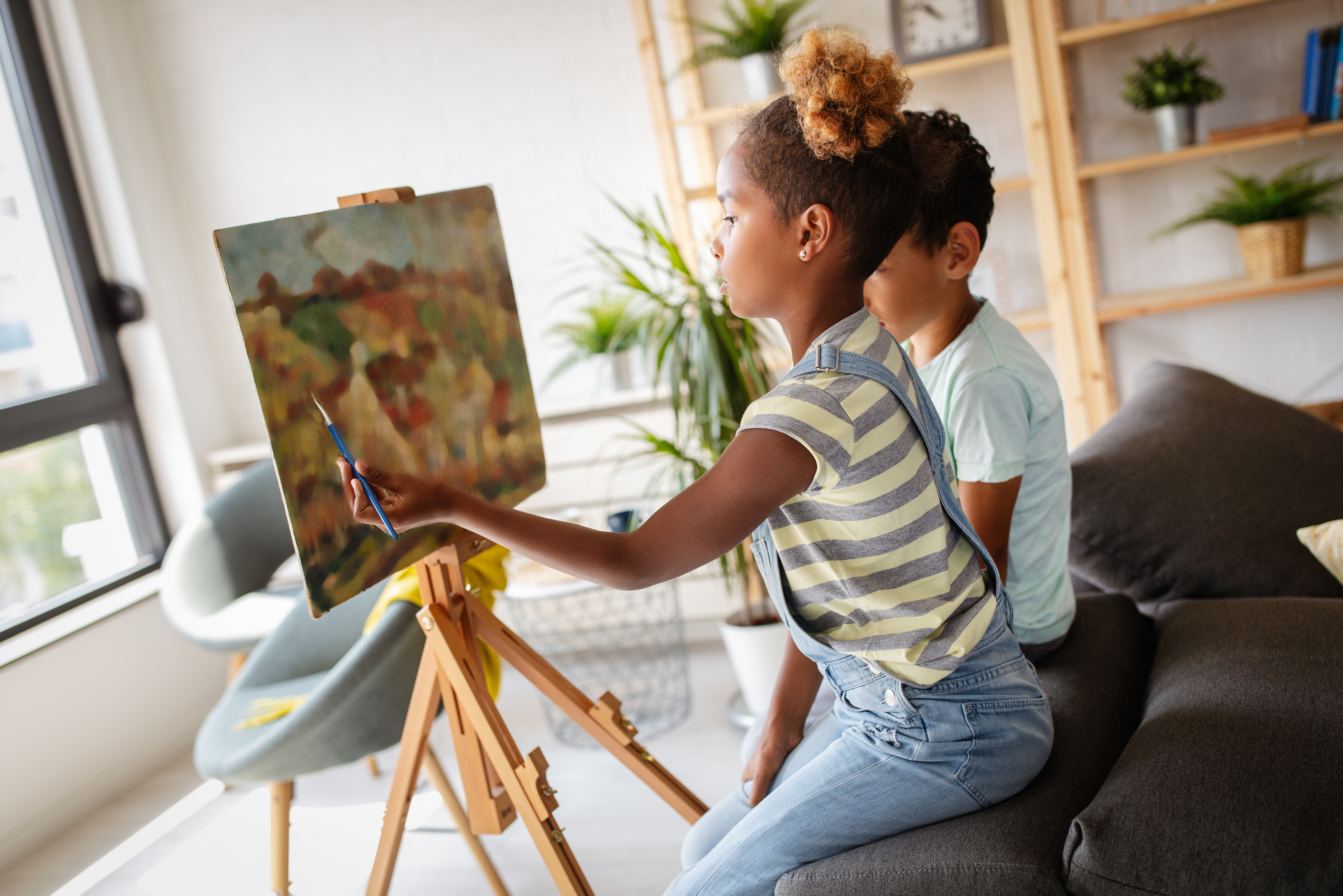 Young girls sits and paints at an easel in her home