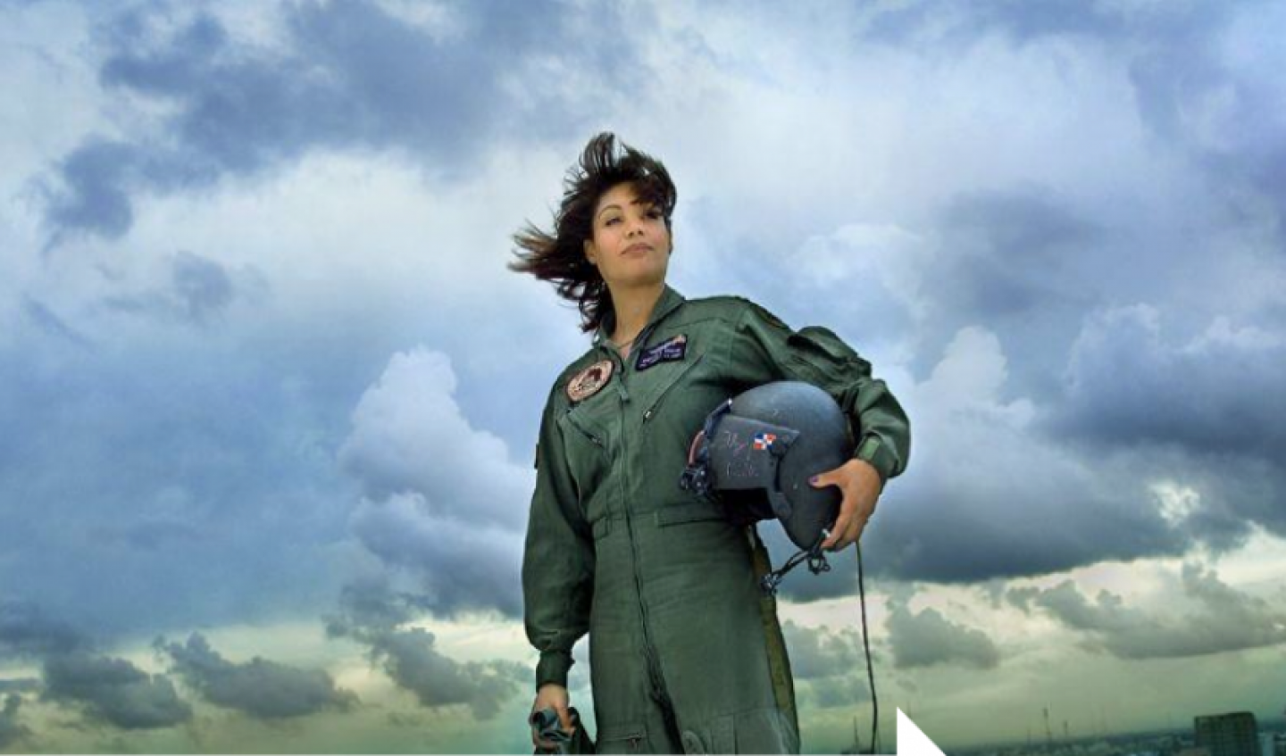 Marisol Chalas wearing her flight uniform and holding a helmet standing against a cloud-filled sky.