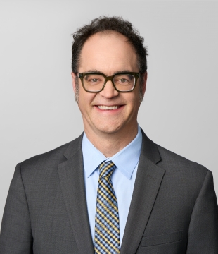 Man wearing a suit and glasses smiles for a headshot