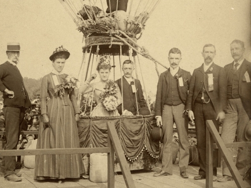 A group stands at a large balloon. A couple is in the basket, with another man standing above them.