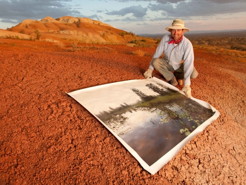 man in red soil holding a picture of a swamp