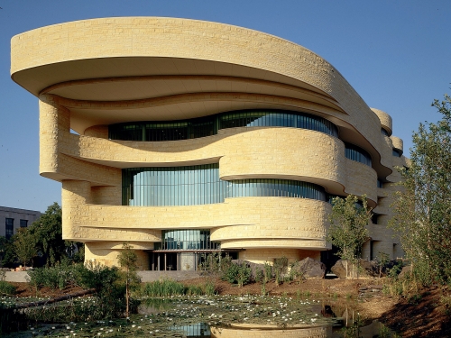 Exterior facade of building with tan stones, windows, and curved sides.