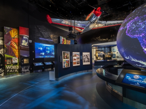 Museum exhibition with hanging airplane and digital screens lining the walls