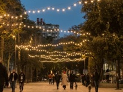 Photograph of brick street with people walking, trees, and string lights.