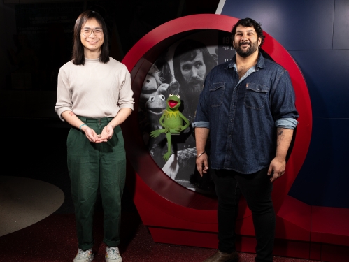 Two people, one holding a small fossilized skull, stand beside green felt puppet, Kermit.