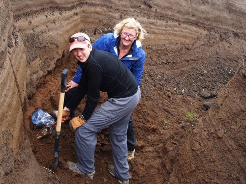 Two people dig for volcanic ash in a ditch using a shovel
