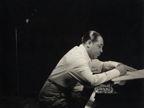 Duke Ellington in profile leaning over an open piano