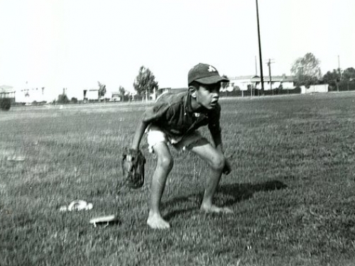 Young boy crouches in a field of grass with a baseball mitt in hand