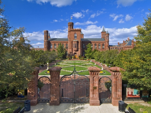 Red sandstone Castle with manicured garden and ornate gate in front