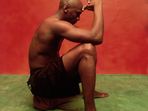 Black man sitting against red wall on green floor