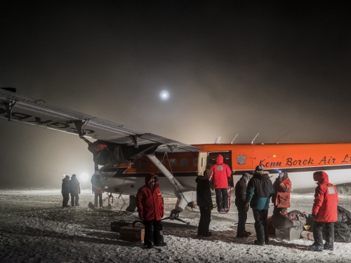 crew in orange parkas loading small plane at night