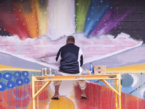 Still image from film Mele Murals showing artist working on rainbow mural