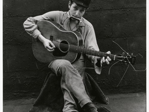 Black and white photo of young Dylan with harmonica and guitar