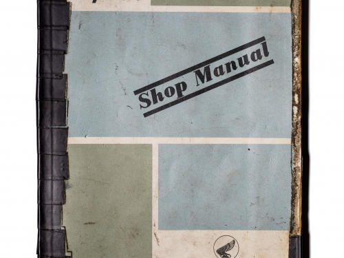 Bound papers with blocks of green and blue and large stamped text saying Shop Manual.