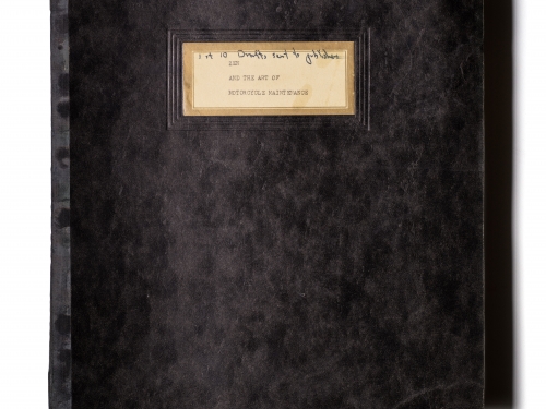 Black, soft-covered book with tan, hand-written label on the cover.