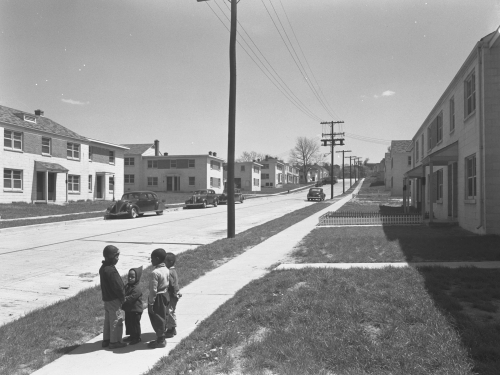Three children stand on sidewalk on barren street