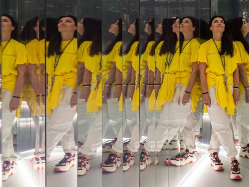 Artist, wearing yellow top and white pants, is reflected in multiple mirrors