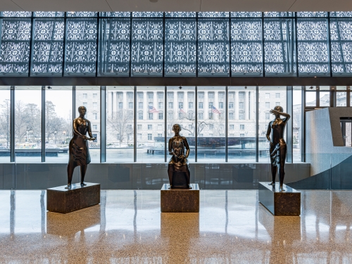 Three sculptures of standing figures on pedestals inside a building