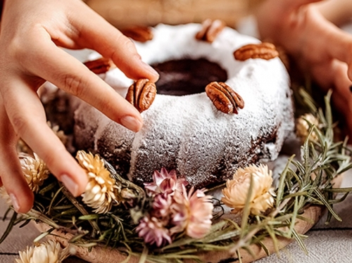 Two hands hover over a bundt cake dusted with powdered sugar.