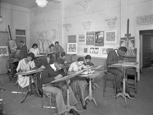 Black and white image of a group of young students sitting at desks in an arts classroom.