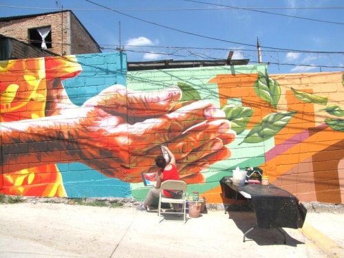 Artist paining a mural of outstretched hands on a wall