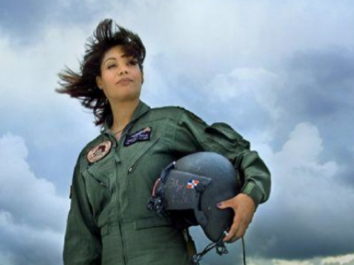 Marisol Chalas wearing her flight uniform and holding a helmet standing against a cloud-filled sky.