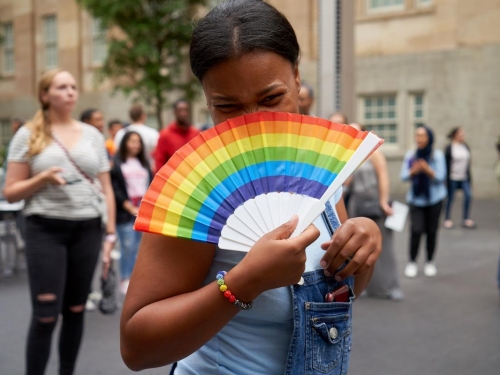 woman holding a rainbow fan up to her face with smiling eyes