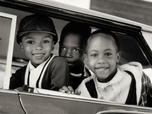 Three Black children smiling at camera from a car. 