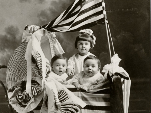 Three children in a wicker baby carriage with an American flag. Black and white photoprint