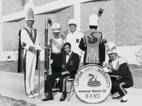 Photograph of William P. Foster and members of the Florida A&M University Marching "100" in uniform around a bass drum.