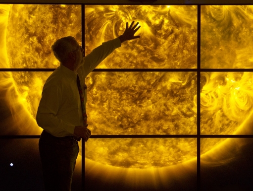 A man stands in front of a series of monitors displaying the surface of the sun.