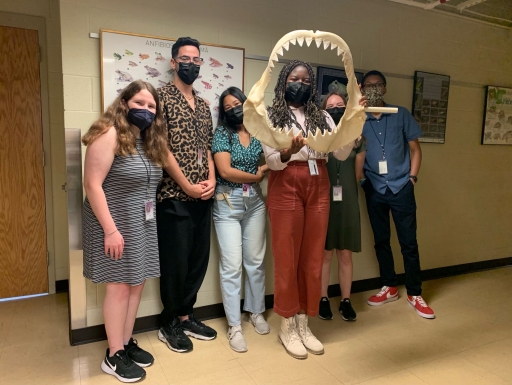 A group of students wearing masks smiles at the camera. One is holding a shark jaw.